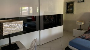 A modern bedroom with a bed, a desk, and a chair. There is a window with blinds, a painting on the wall, and a small table with a lamp. - Villa Alfonso with sea view (Siculiana)