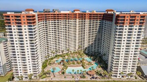 Un hôtel de grande hauteur doté de nombreux balcons, d’une cour intérieure avec une piscine et offrant une vue sur la plage.