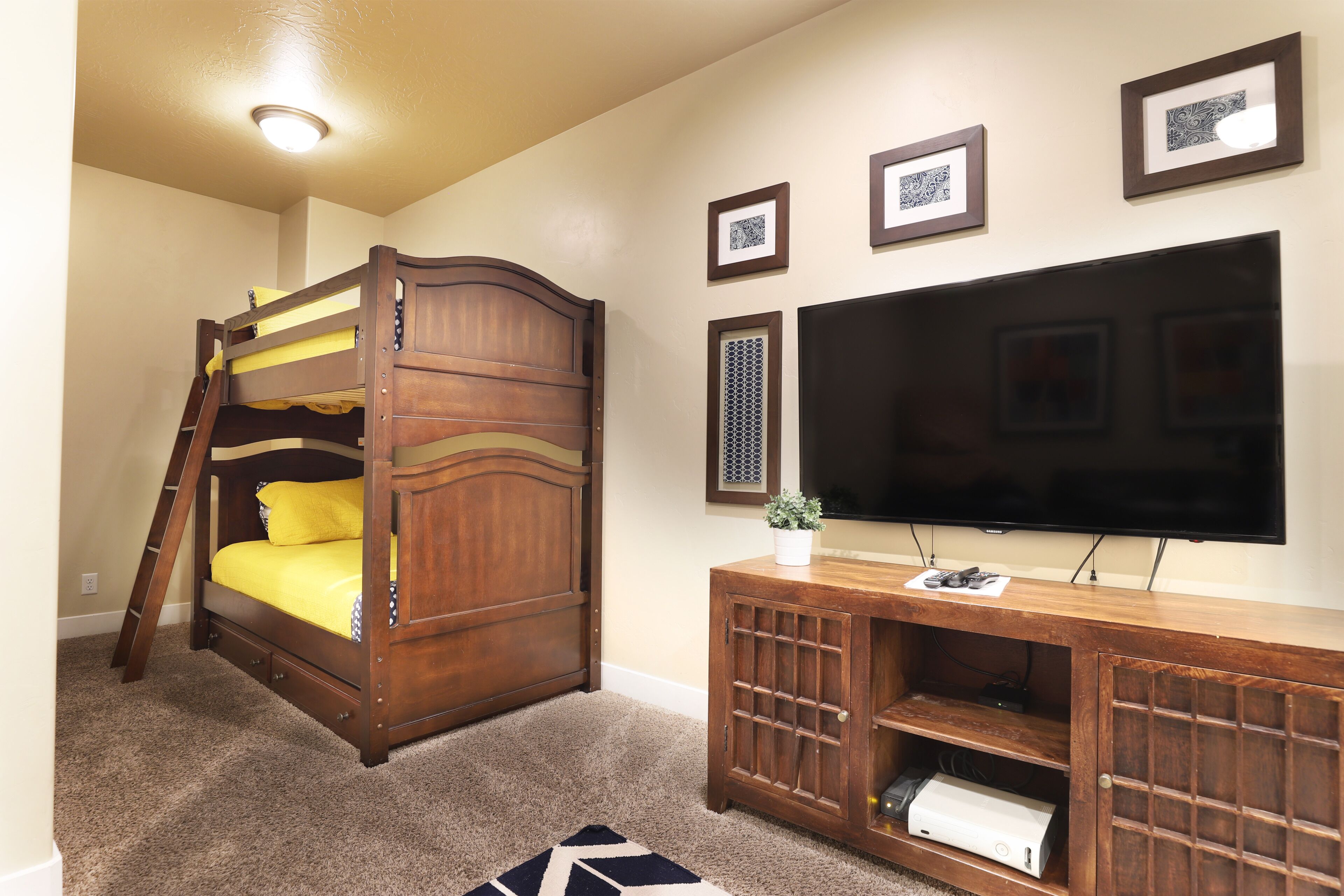 A bedroom with a bunk bed, a TV mounted on the wall, and a wooden entertainment unit.