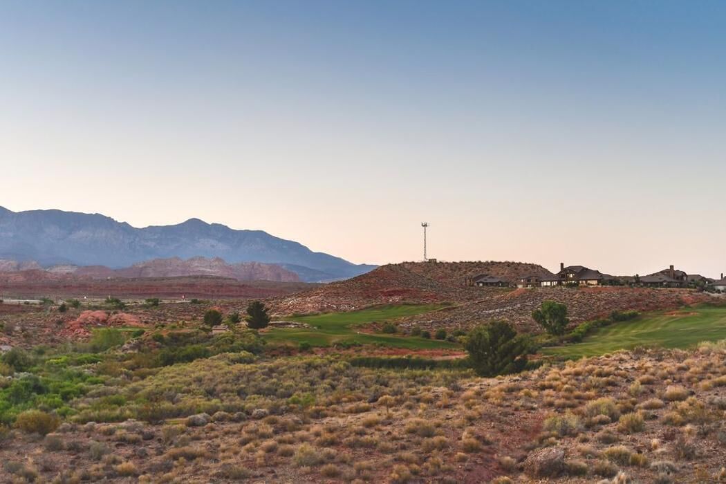 A desert landscape with a golf course, a few buildings, and mountains in the background.