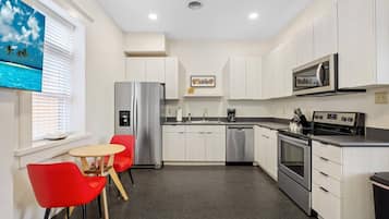 A modern kitchen with white cabinets, stainless steel appliances, a red chair, and a painting of a beach scene.