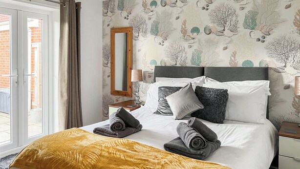 A hotel room with a bed, a mirror, a nightstand, and a view of the outside. - 2 bedroom accommodation in Bridlington (Bridlington)