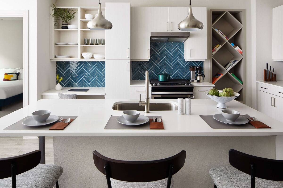 A modern kitchen with white cabinetry, a central island with seating, and a blue herringbone backsplash.