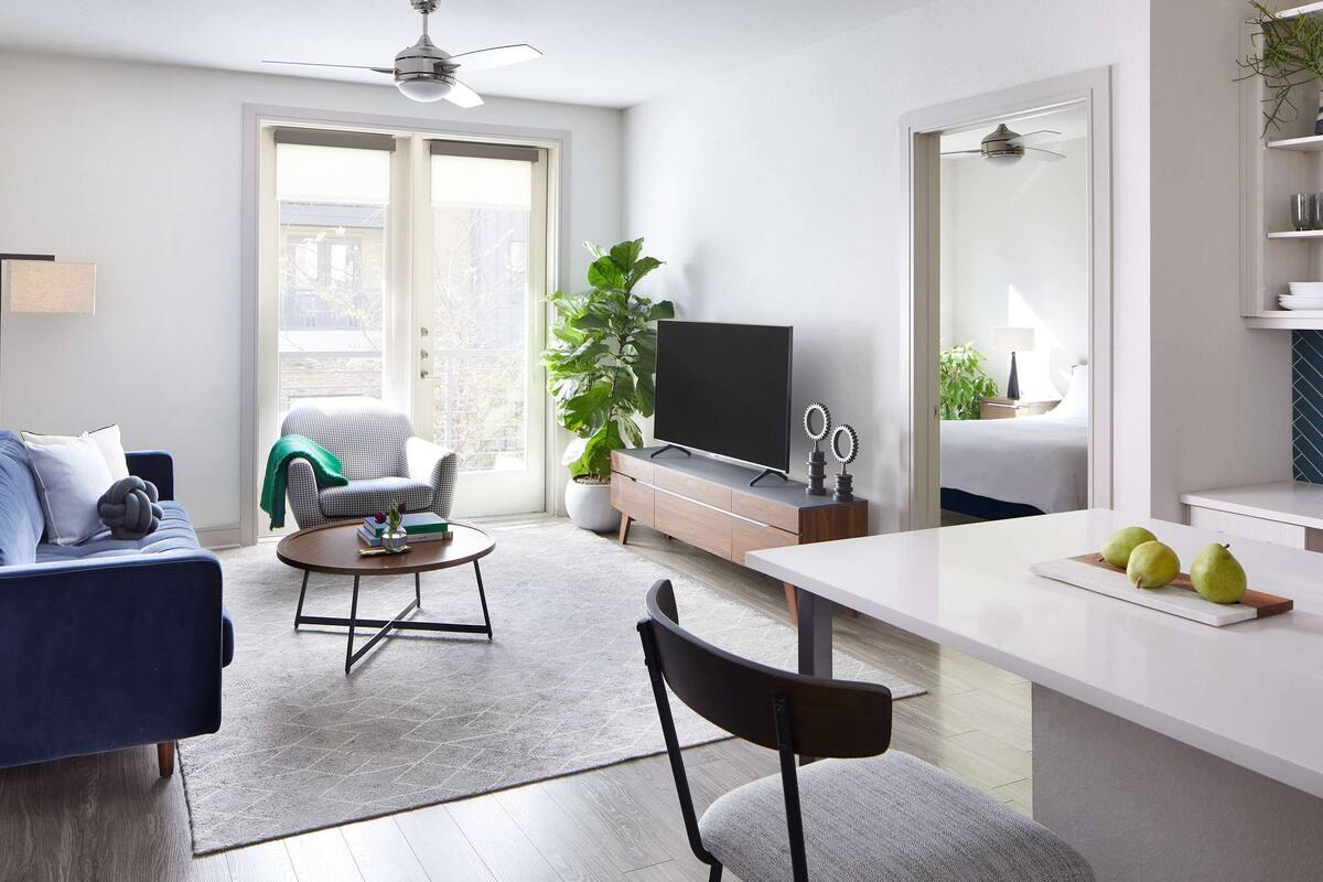 A modern living room with a sofa, a coffee table, a TV, and a dining area with a table and chairs.