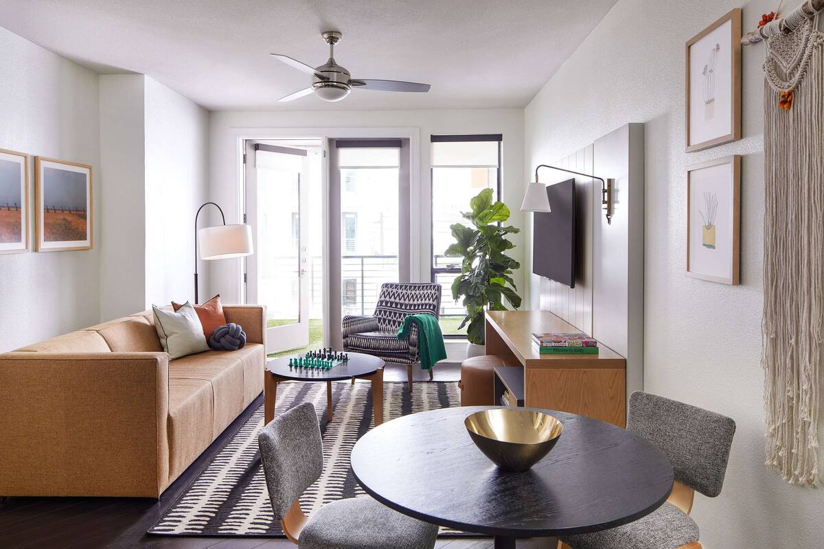 A modern living room with a sofa, chairs, a coffee table, a TV, and a large window.