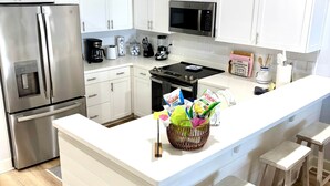 Une cuisine moderne avec des meubles blancs, des appareils en acier inoxydable et un îlot central doté de tabourets.