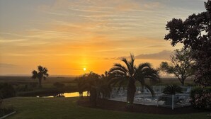 Un coucher de soleil sur un champ herbeux, avec une clôture et des arbres.