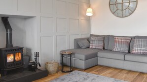 A modern living room with a fireplace, grey sofa, and a round mirror on the wall. - 4 bedroom accommodation in West Bennan, near Shannochie (West Bennan, near Shannochie)