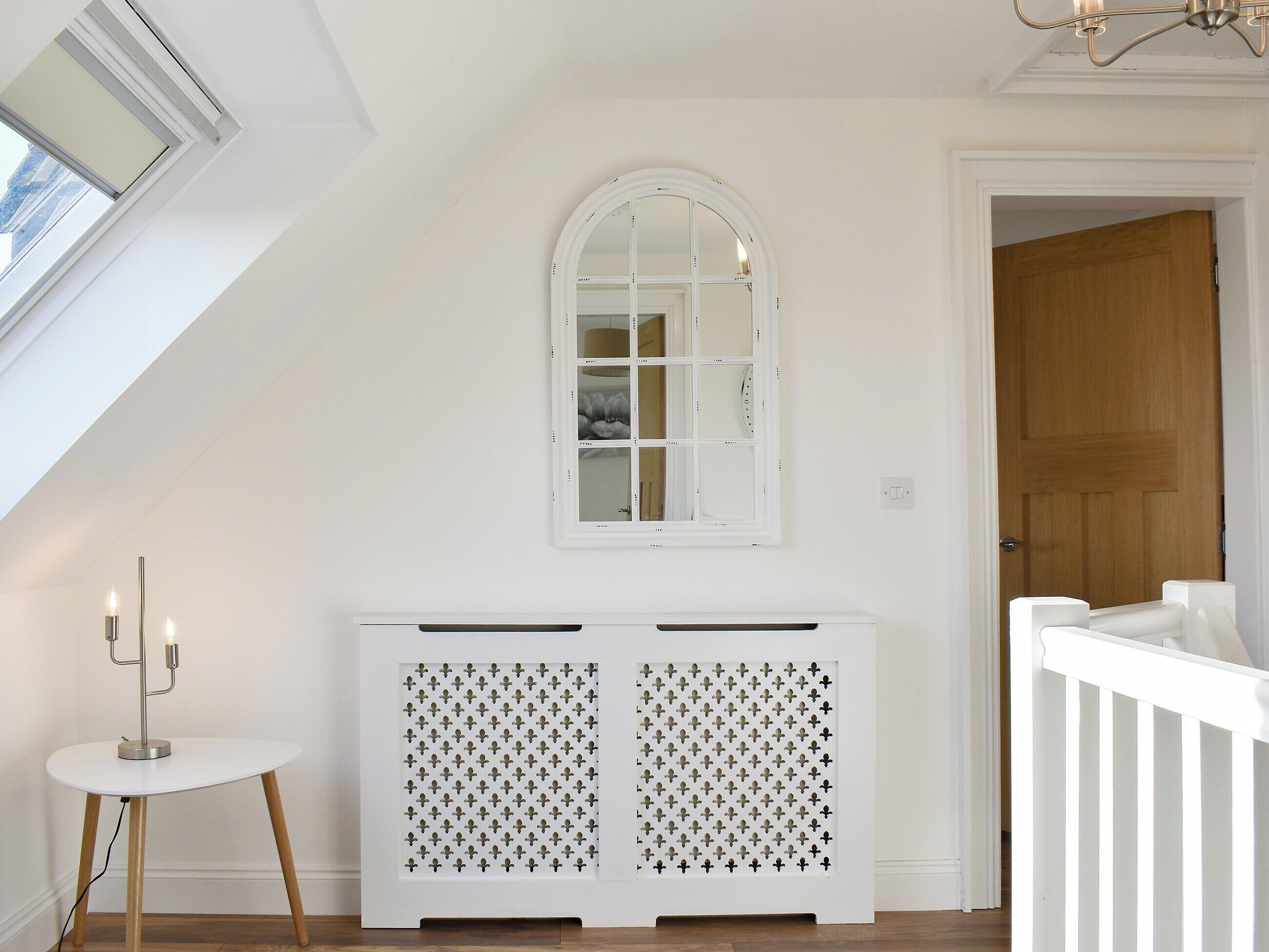 Een witte console tafel met een decoratief paneel, een spiegel erboven en een klein tafeltje met kaarsen.
