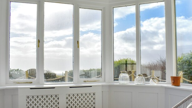 A bay window with a table set for tea, a wicker chair, and a view of the sky and greenery outside. - 4 bedroom accommodation in West Bennan, near Shannochie (West Bennan, near Shannochie)