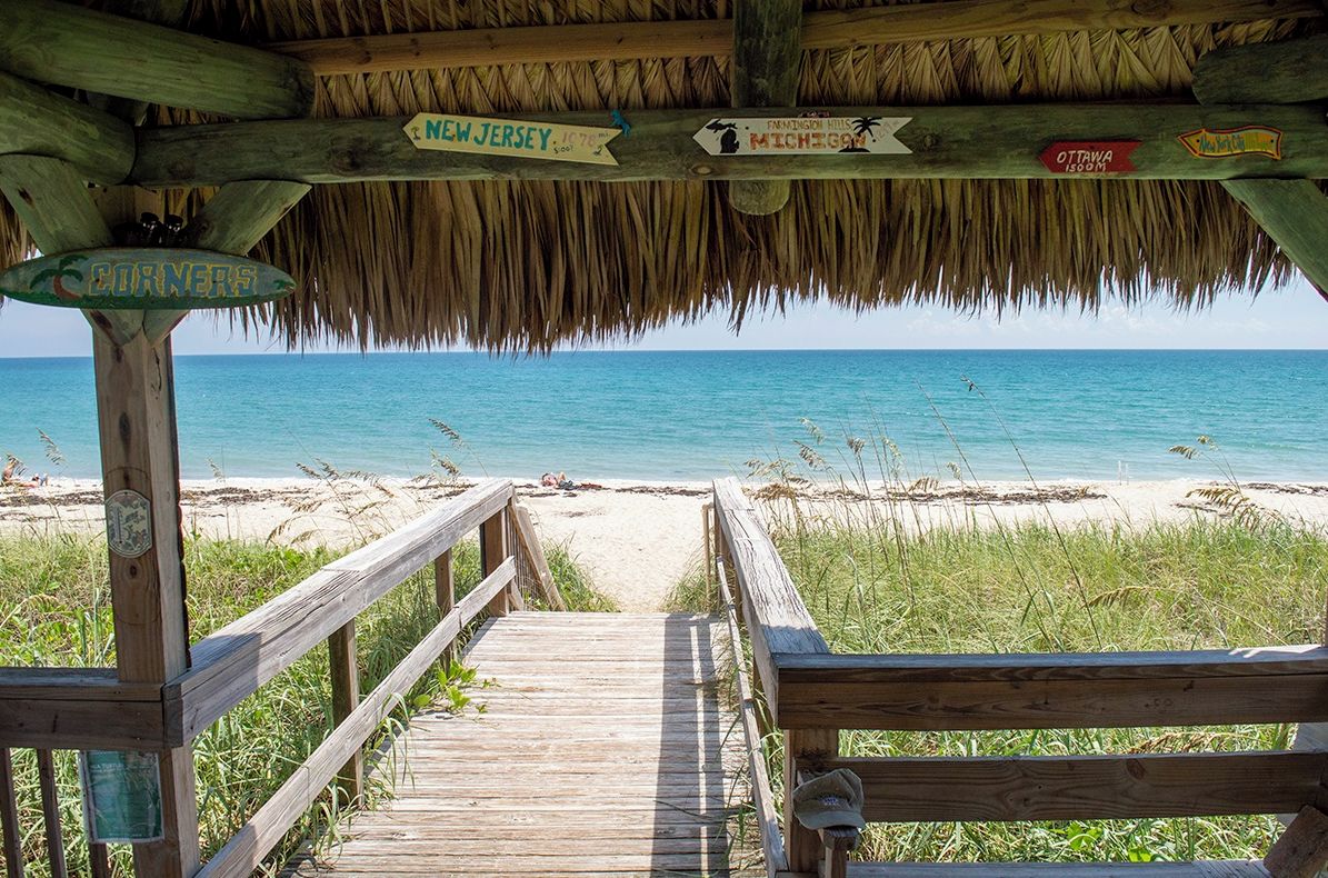 A wooden boardwalk leading to a beach with directional signs indicating nearby locations.