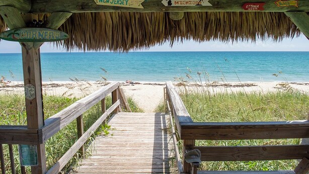 A wooden boardwalk leading to a beach with directional signs indicating nearby locations.