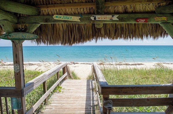 Un muelle de madera que conduce a una playa, con señales indicando lugares cercanos.