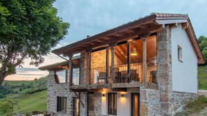 A two-story stone house with a balcony, large windows, and a patio area.