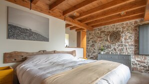 A bedroom with a wooden headboard, a stone wall, and a bed with white bedding.
