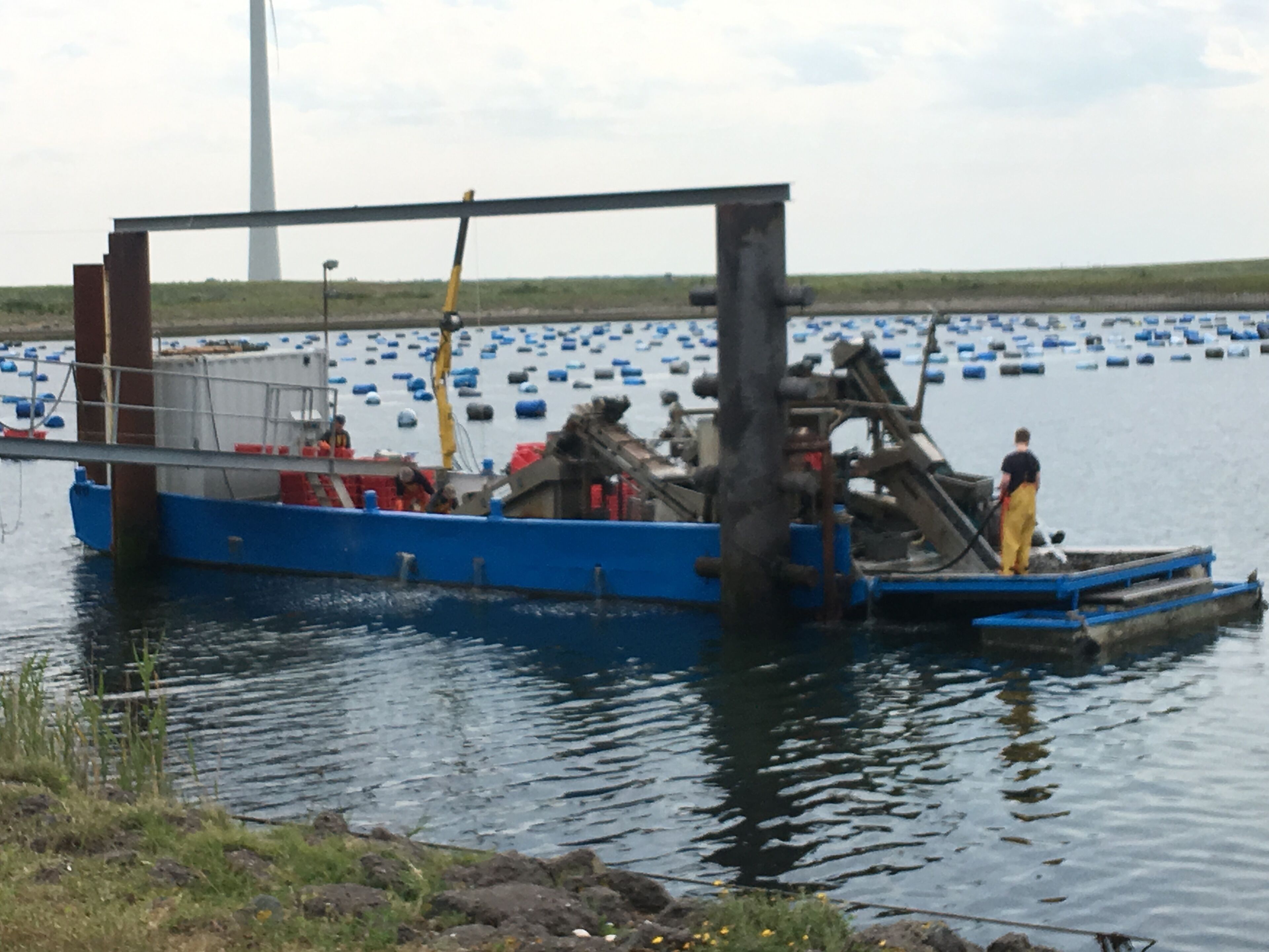 A blue boat docked at a pier with a large wind turbine in the background.