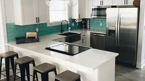Une cuisine moderne avec des meubles blancs, un réfrigérateur en acier inoxydable, un four encastré et un îlot central doté de tabourets de bar.