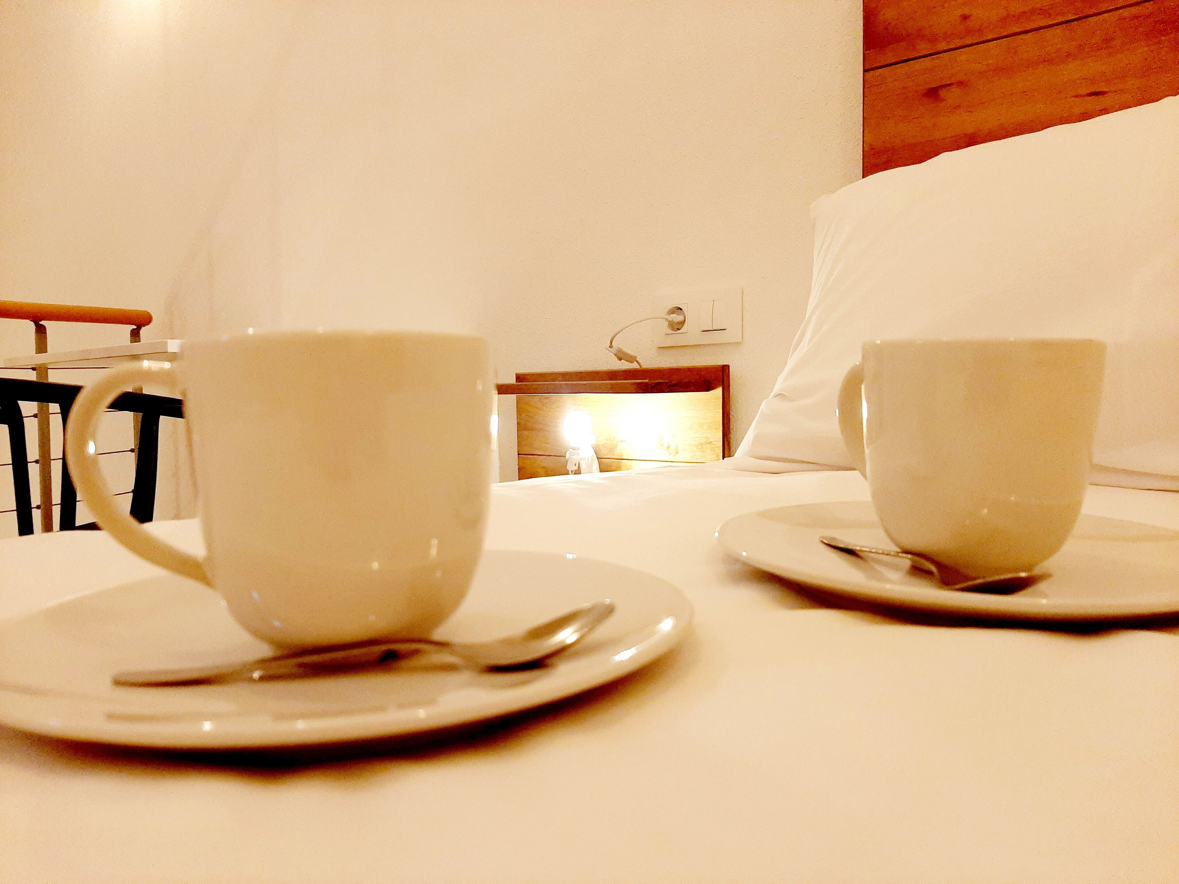 Two white cups on saucers on a white table in a hotel room.