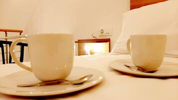 Two white cups on saucers on a white table in a hotel room.