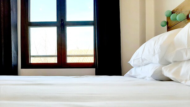 Una cama con ropa de cama blanca, una ventana con vistas a un edificio y una pared con un adorno decorativo verde.
