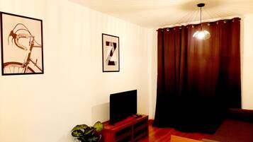Un salón con un televisor sobre un mueble de madera, una planta en maceta y una letra Z enmarcada en la pared.