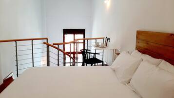 Habitación de hotel con cama, una mesita con cafetera, una silla y una escalera que lleva a otra habitación.