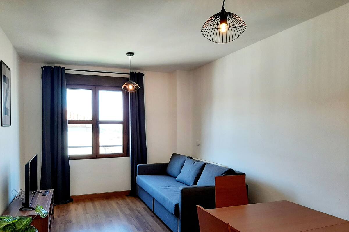 A compact living space with a sofa, a dining table, a TV, and a window with curtains.