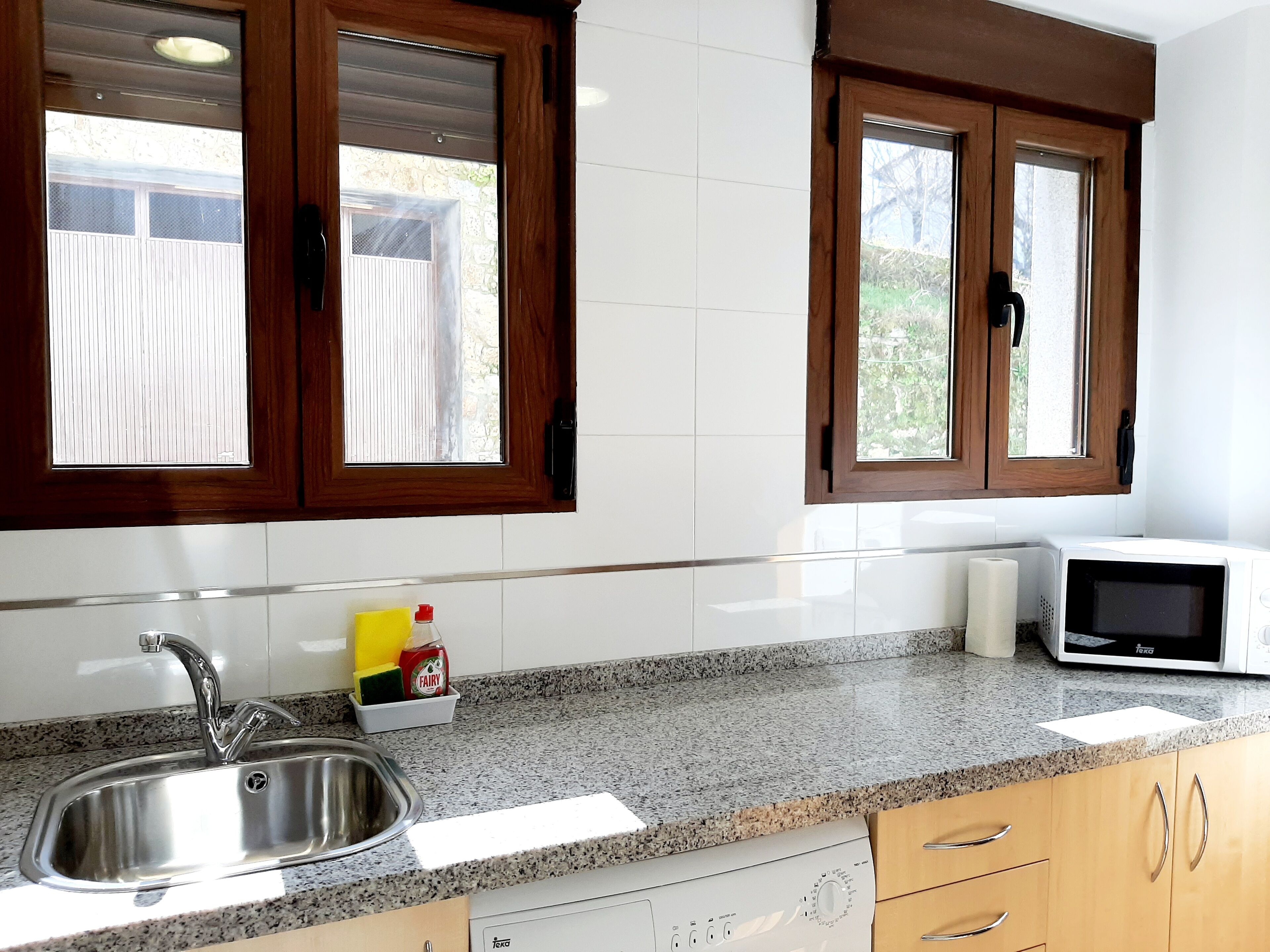 Una cocina con pileta de acero inoxidable, encimera de granito, muebles de madera y microondas.