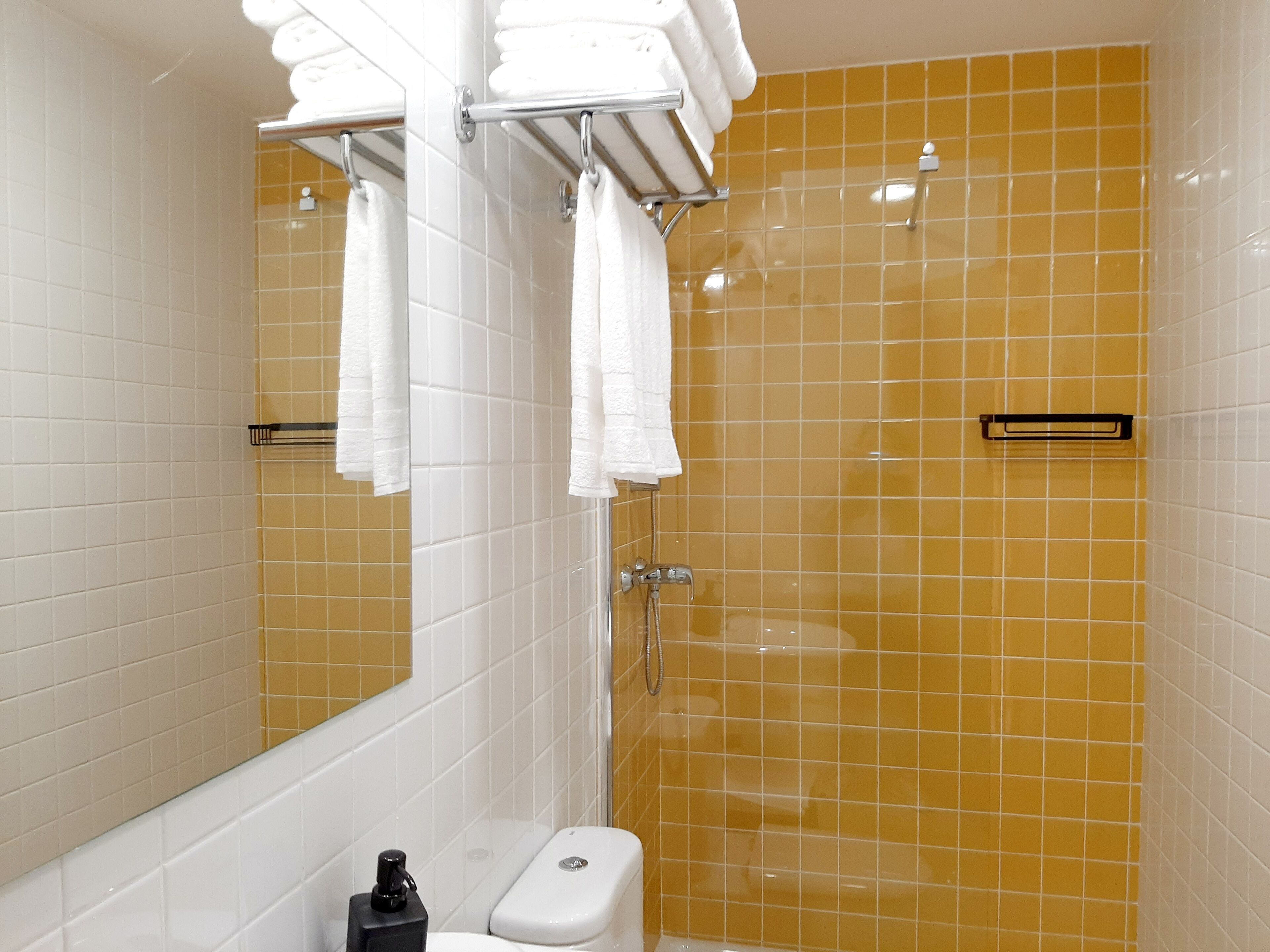 Een badkamer met witte en gele tegels, een toilet, een wastafel en een spiegel.