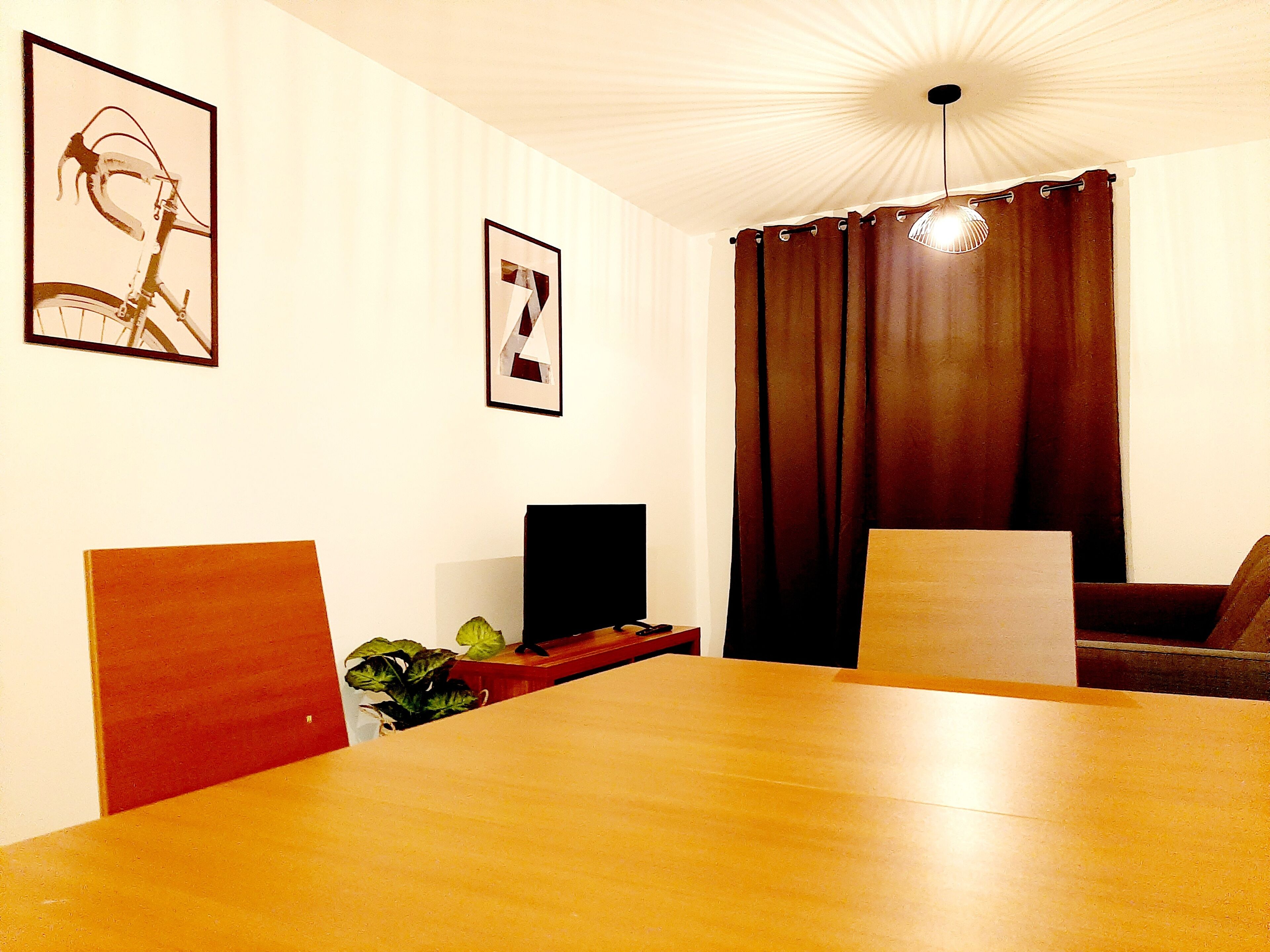 Un espace repas comprenant une table en bois, des chaises, un téléviseur et des œuvres d’art encadrées accrochées aux murs.