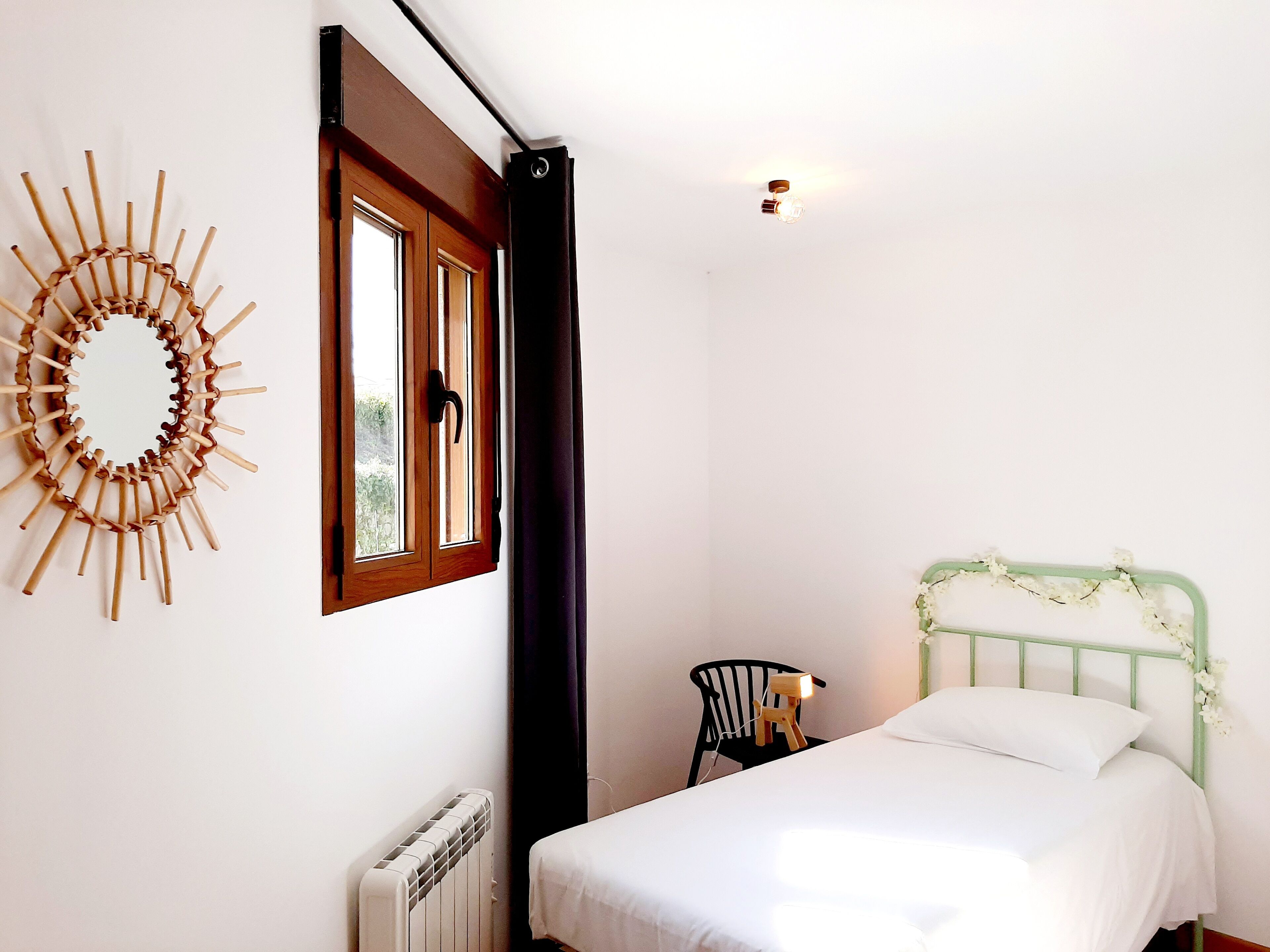 A bedroom with a bed, a radiator, a chair, a window with a curtain, and a wall decoration.