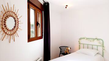 A bedroom with a bed, a radiator, a chair, a window with a curtain, and a wall decoration.