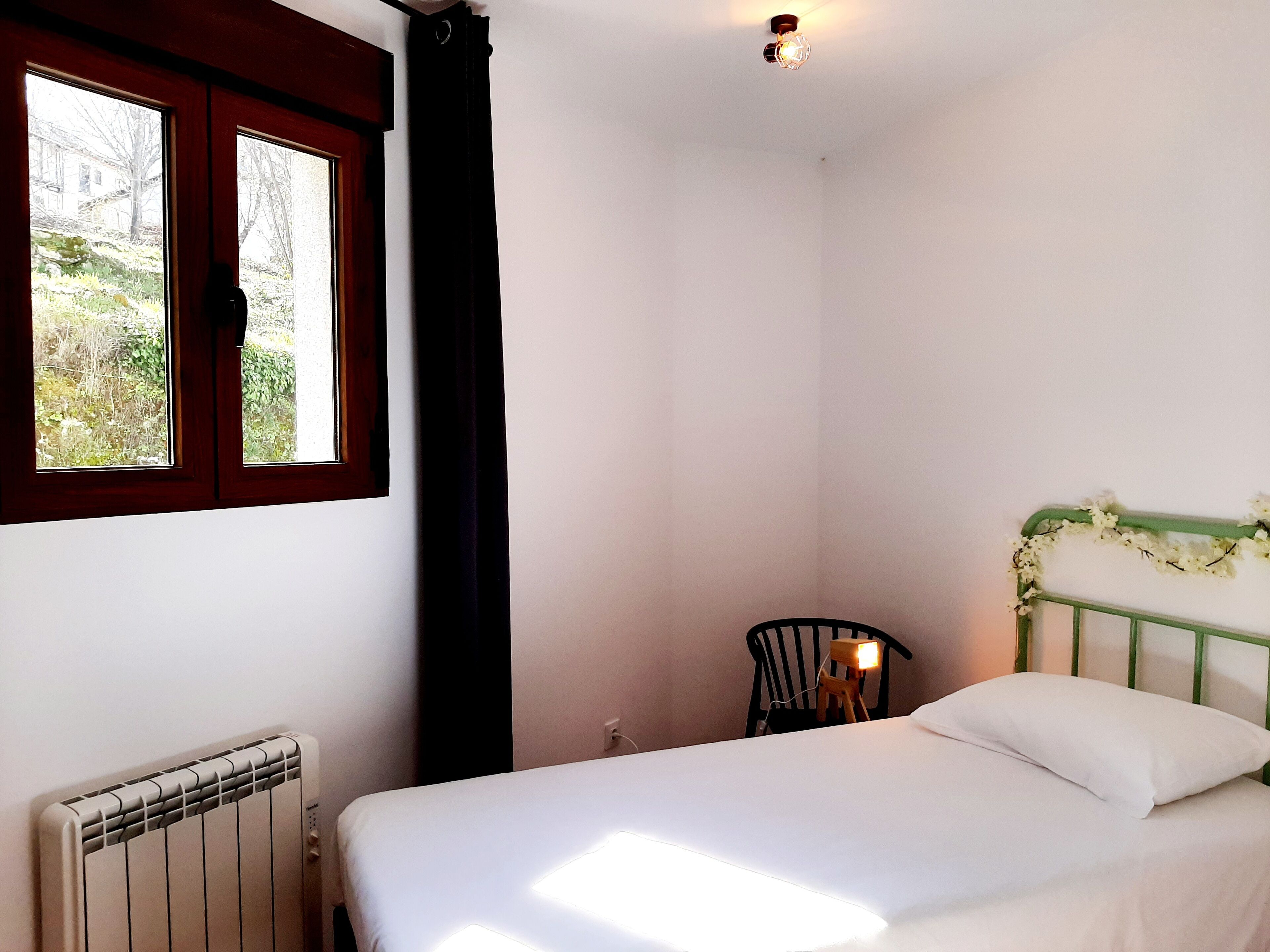 Une chambre à coucher avec un lit, un radiateur, une fenêtre avec des rideaux et une chaise.