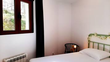 Une chambre à coucher avec un lit, un radiateur, une fenêtre avec des rideaux et une chaise.