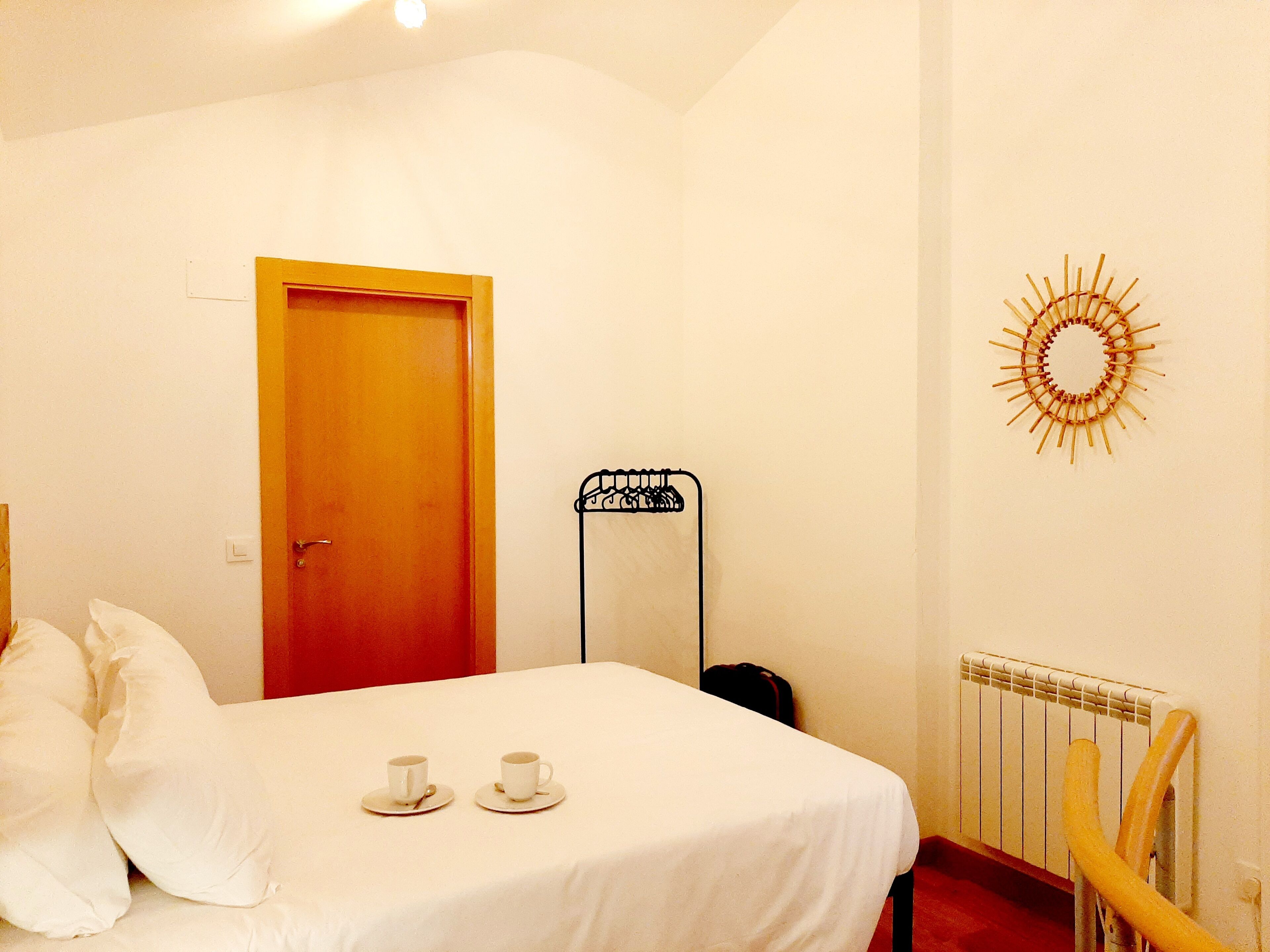 A bedroom with a bed, two cups on a tray, a radiator, and a door.