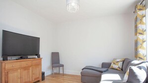 Una sala moderna con televisor de pantalla plana, mueble de madera, sofá gris y cortina estampada.