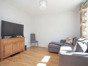 A modern living room with a flat-screen TV, wooden cabinet, grey sofa, and a patterned curtain. - 5 bedroom accommodation in Crantock, near Newquay (Crantock, near Newquay)