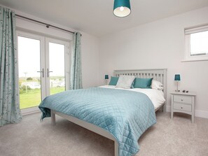 A bedroom with a bed, a nightstand, a lamp, and a view through a window. - 5 bedroom accommodation in Crantock, near Newquay (Crantock, near Newquay)