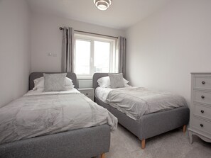 A bedroom with two single beds, a dresser, a window with curtains, and a radiator. - 5 bedroom accommodation in Crantock, near Newquay (Crantock, near Newquay)
