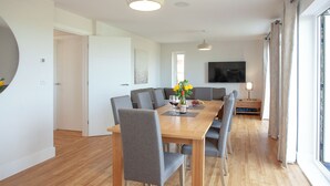 Un comedor moderno con una mesa de madera, sillas tapizadas en gris y un amplio ventanal con cortinas.