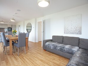 A modern living room with a wooden dining table, grey upholstered chairs, a grey sofa with a furry throw, and a large abstract painting on the wall. - 5 bedroom accommodation in Crantock, near Newquay (Crantock, near Newquay)