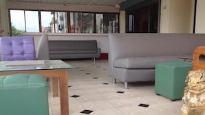 Una habitación con una mesa de vidrio, una silla morada, un sofá gris, un otoman verde y una estatua decorativa de león.