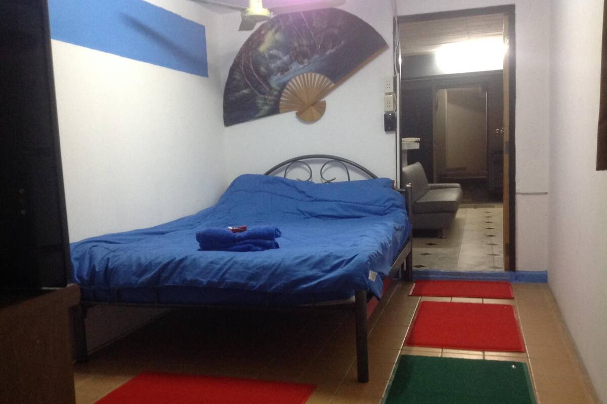 Une chambre à coucher comprenant un lit, un ventilateur, une chaise et une porte donnant sur une autre pièce.