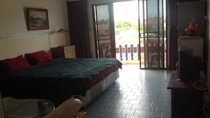 Habitación de hotel con cama, escritorio con silla, televisor y puerta corrediza de vidrio que da a un espacio exterior.