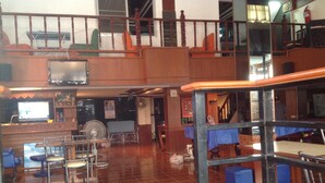 Un hall amplio con techo alto, una escalera y una zona de estar con sillas y mesas.