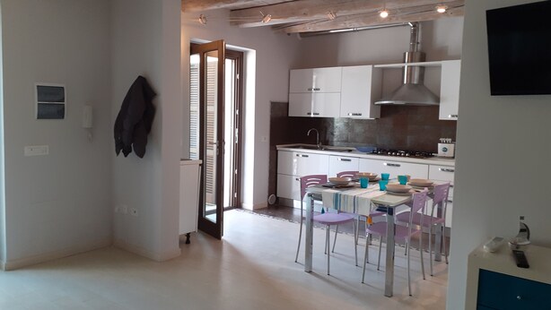 Een moderne keuken met witte kastjes, een gasfornuis en een spoelbak. Er is een eethoek met een tafel en stoelen.