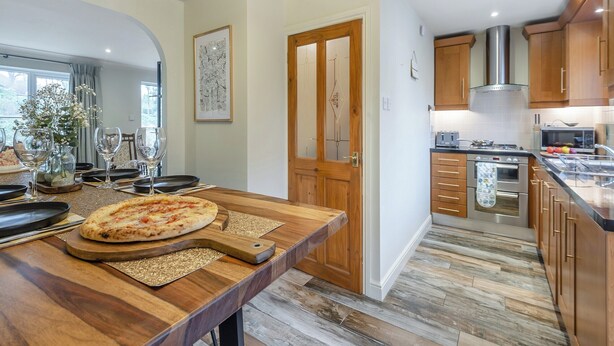 A modern kitchen with wooden cabinets, a built-in oven, and a dining area with a wooden table set for two.