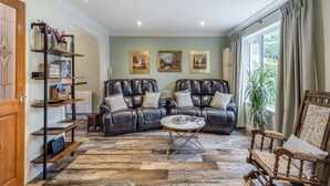 A living room with two leather sofas, a coffee table, and a wooden rocking chair. There are bookshelves, a radiator, and two framed pictures on the wall.