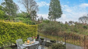 A patio with a table and chairs, surrounded by greenery and a fence.