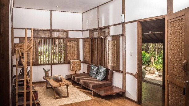 Una tradizionale stanza in stile giapponese con pavimento in tatami, una panca di legno bassa, un cesto intrecciato e una porta scorrevole che dà su un'area esterna.